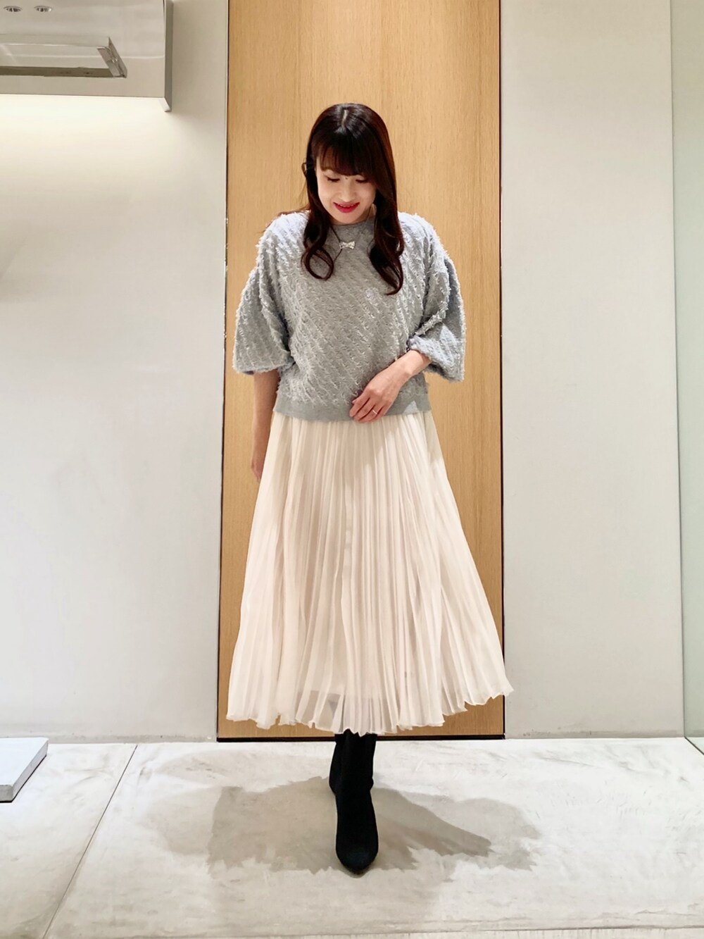 グレー系のニット/セーター、ホワイト系のスカート、シルバー系のネックレスを着用したレディースの秋コーディネートの2枚目の写真