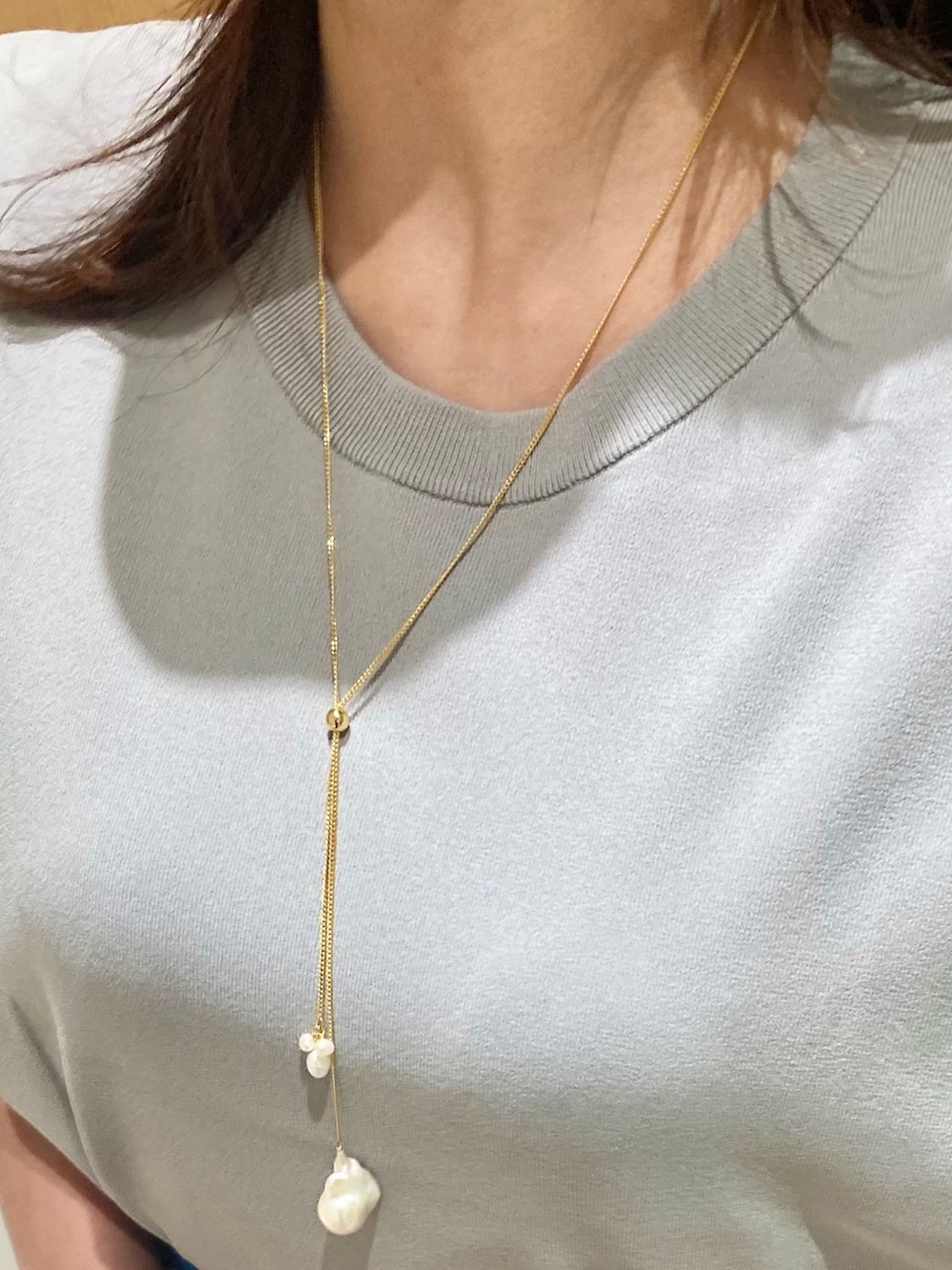 グレー系のニット/セーター、ブルー系のスカート、ホワイト系のネックレスを着用したレディースの夏コーディネートの5枚目の写真