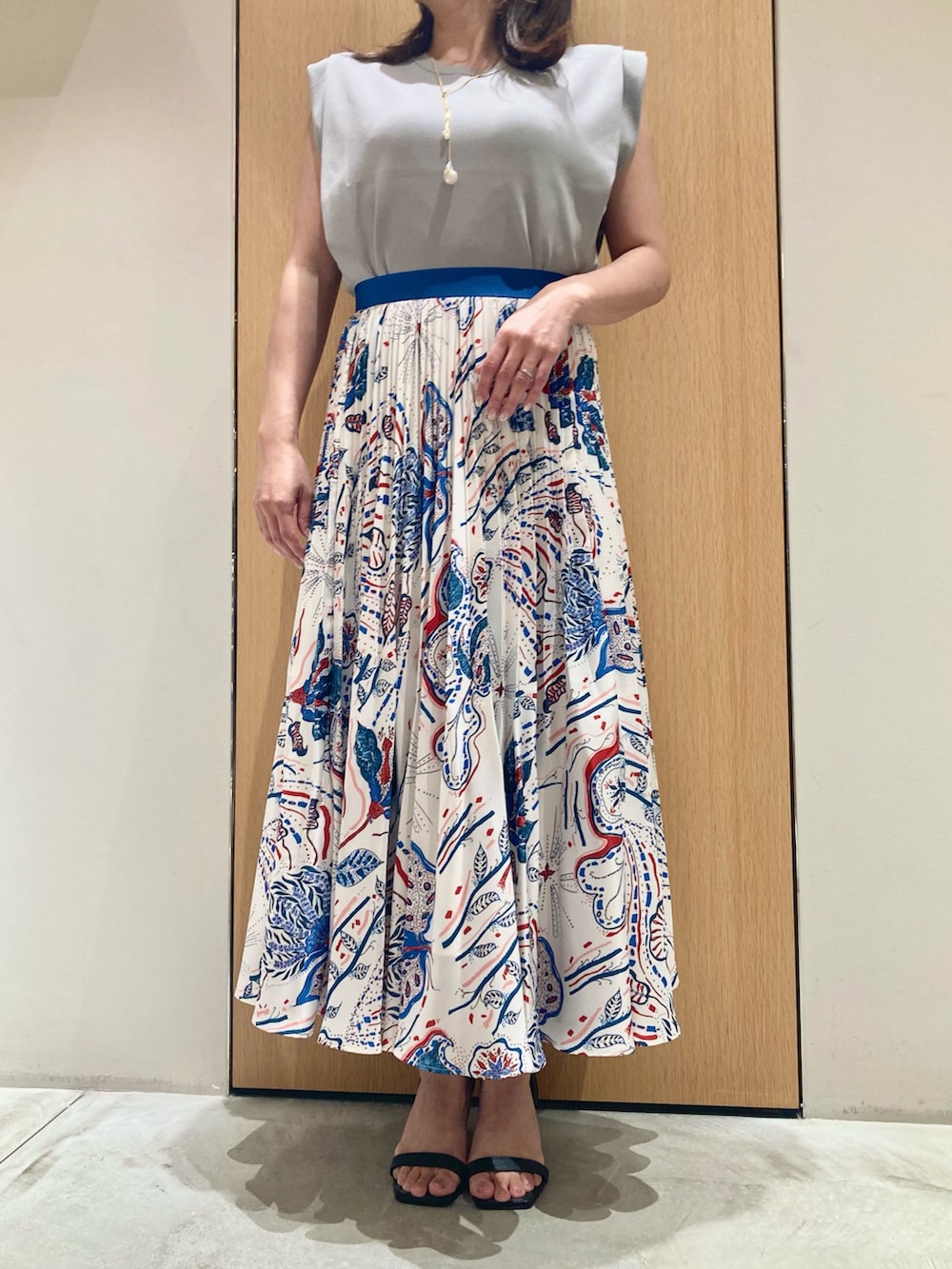 グレー系のニット/セーター、ブルー系のスカート、ホワイト系のネックレスを着用したレディースの夏コーディネートの4枚目の写真