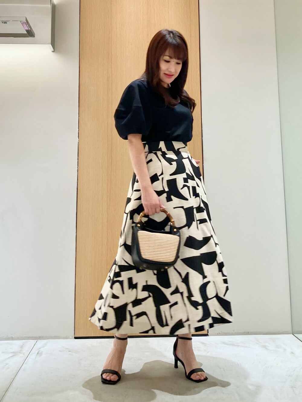 ブラック系のTシャツ/カットソー、ベージュ系のスカート、ブラック系のハンドバッグを着用したレディースの春コーディネートの2枚目の写真