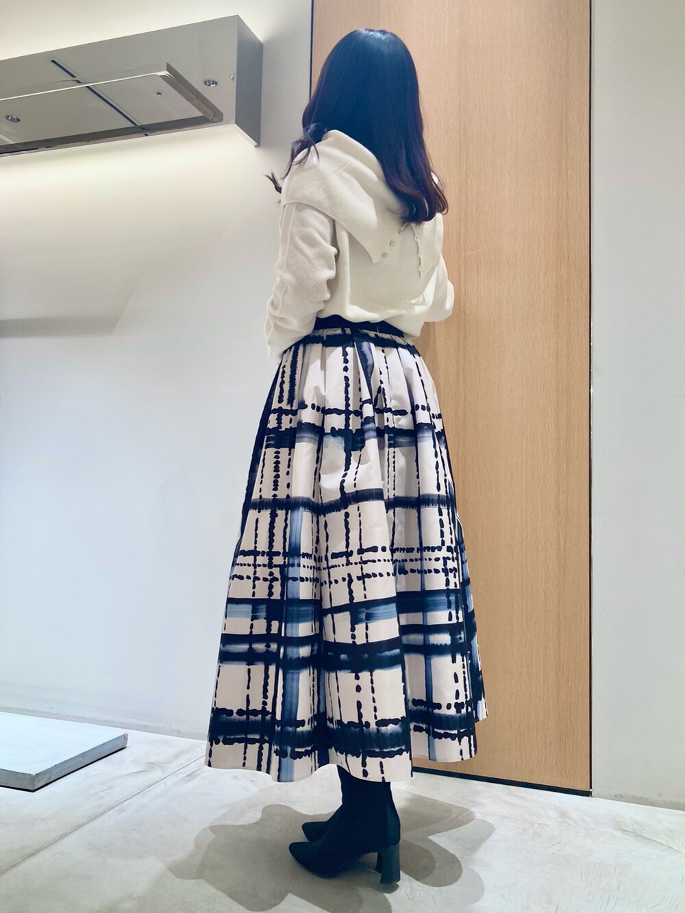 ホワイト系のニット/セーター、ホワイト系のスカート、ブラック系のイヤリングを着用したレディースの秋コーディネートの6枚目の写真