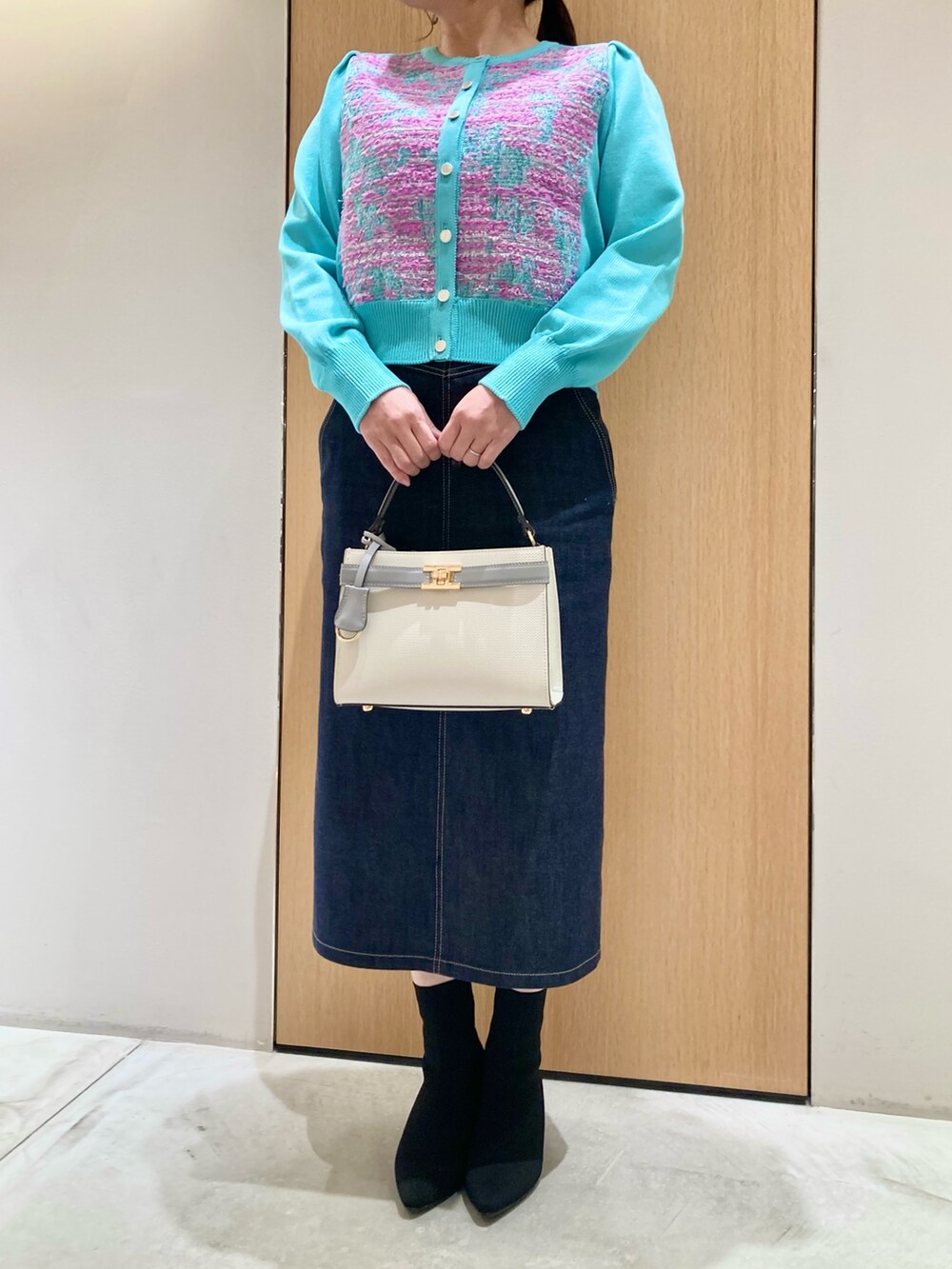 グリーン系のカーディガン/ボレロ、ホワイト系のハンドバッグ、ブルー系のデニムスカートを着用したレディースの冬コーディネートの3枚目の写真