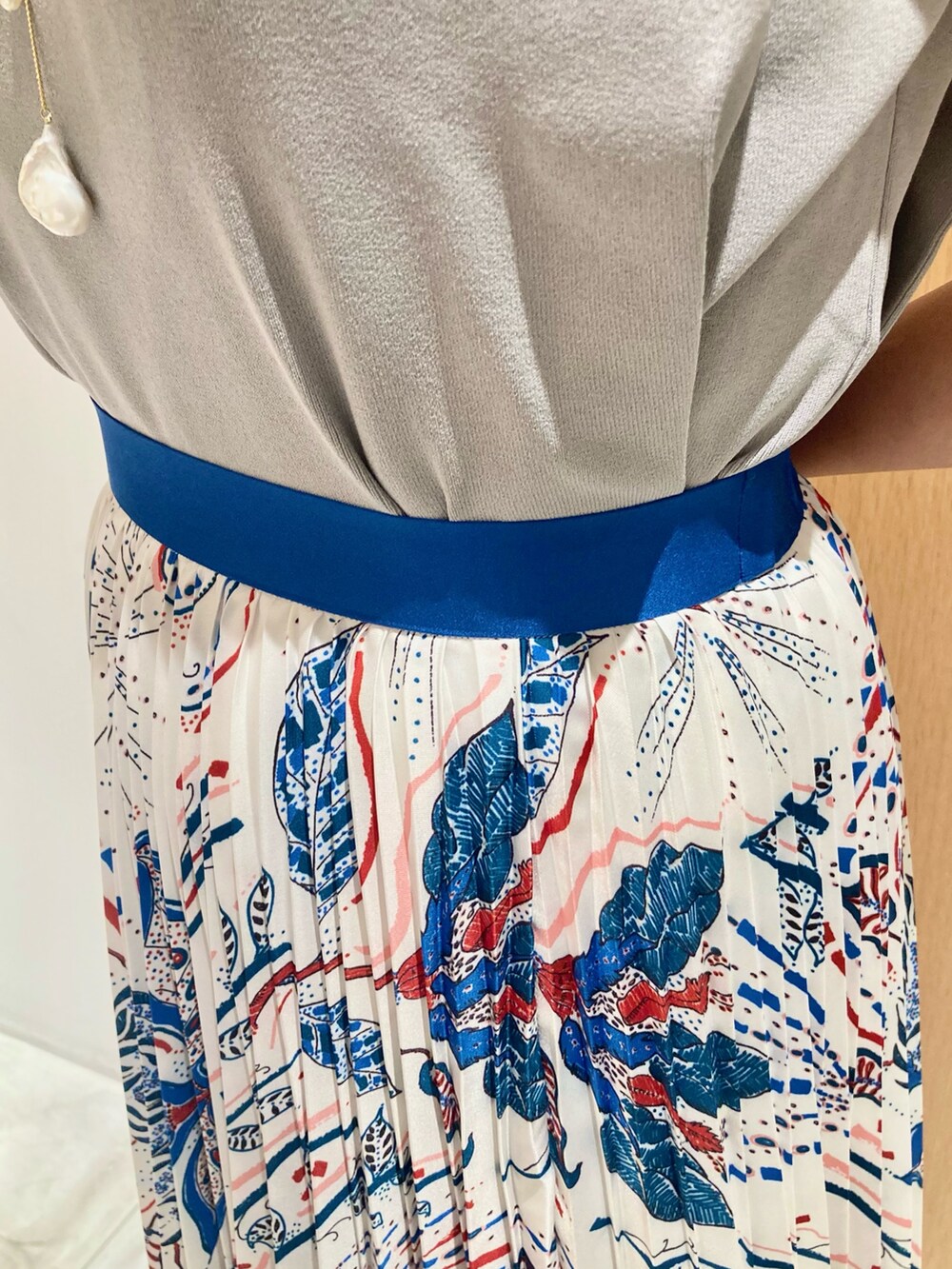 グレー系のニット/セーター、ブルー系のスカート、ホワイト系のネックレスを着用したレディースの夏コーディネートの7枚目の写真