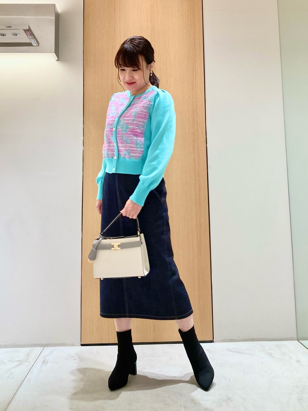 グリーン系のカーディガン/ボレロ、ホワイト系のハンドバッグ、ブルー系のデニムスカートを着用したレディースの冬コーディネートの2枚目の写真
