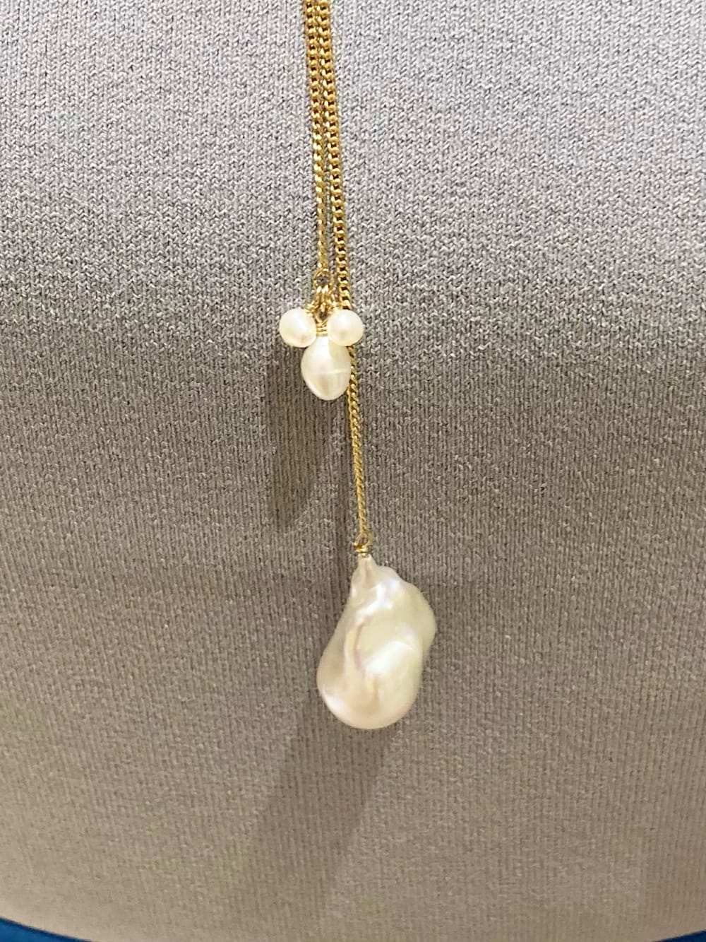 グレー系のニット/セーター、ブルー系のスカート、ホワイト系のネックレスを着用したレディースの夏コーディネートの6枚目の写真