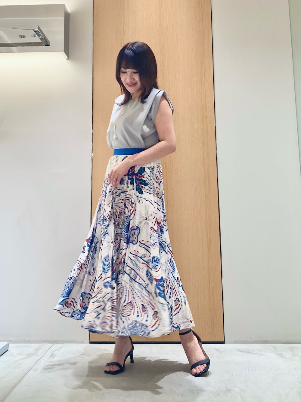 グレー系のニット/セーター、ブルー系のスカート、ホワイト系のネックレスを着用したレディースの夏コーディネートの2枚目の写真