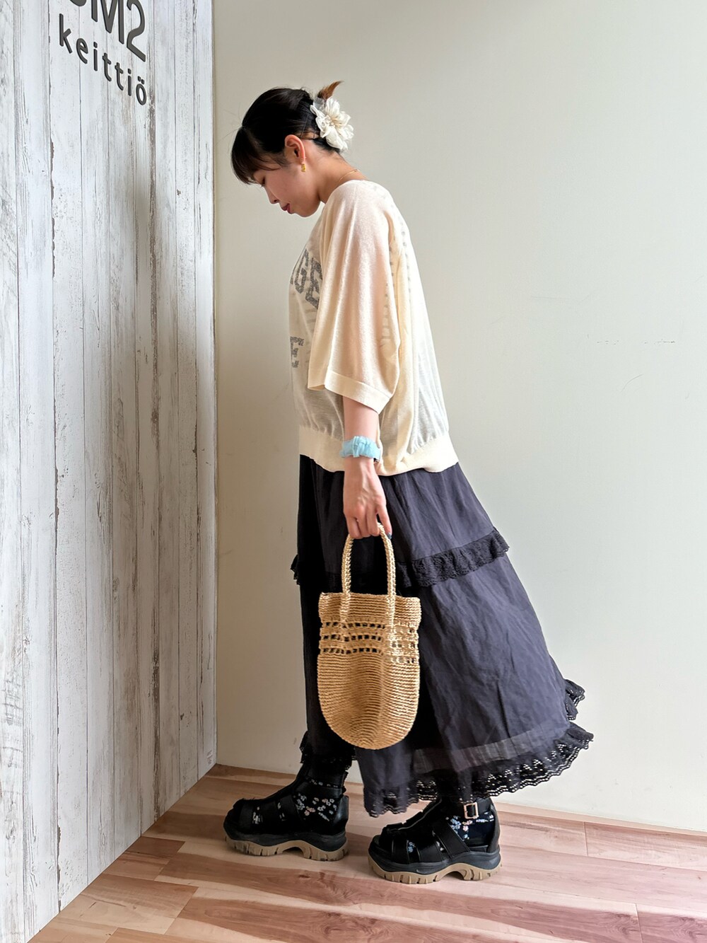 ゴールド系のハンドバッグ、ブラック系のスカート、グリーン系のニット/セーターを着用したレディースの春コーディネートの2枚目の写真