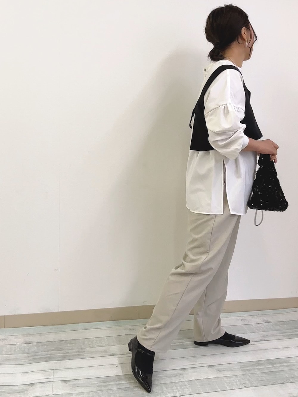 ブラック系のベスト、ブラック系のハンドバッグ、ベージュ系のスラックスを着用したレディースの春コーディネートの2枚目の写真