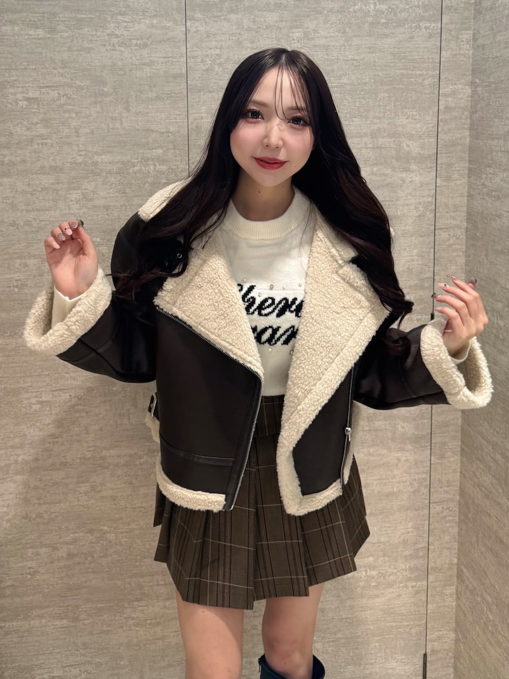 ブラウン系のムートンコート、ホワイト系のニット/セーター、ブラウン系のスカートを着用したレディースの秋コーディネートの3枚目の写真