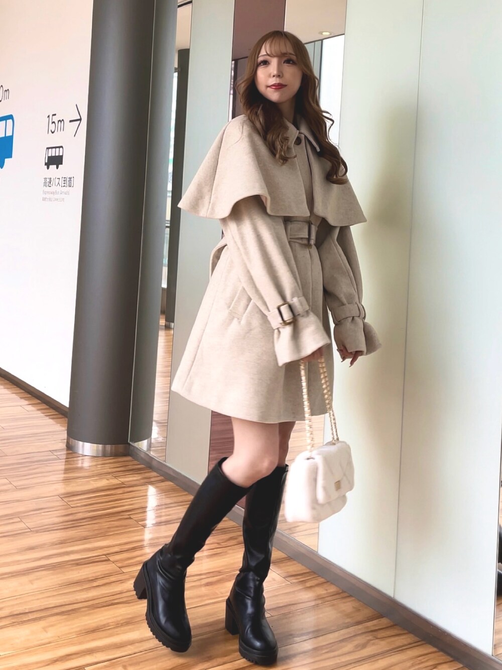 ベージュ系のステンカラーコート、ホワイト系のショルダーバッグ、ブラック系のブーツを着用したレディースの冬コーディネートの2枚目の写真