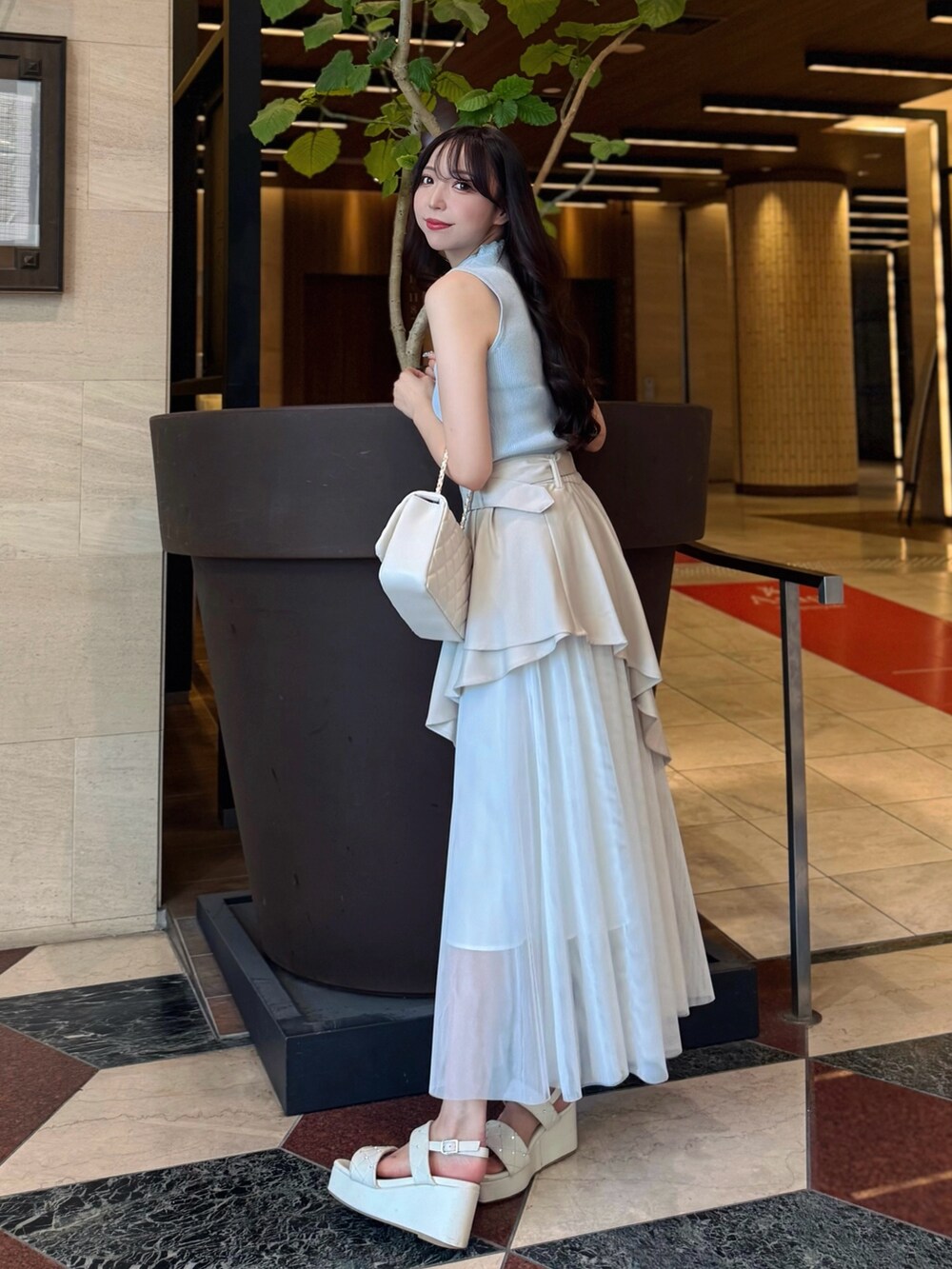 ベージュ系のスカート、ブルー系のニット/セーター、ホワイト系のショルダーバッグを着用したレディースの夏コーディネートの3枚目の写真