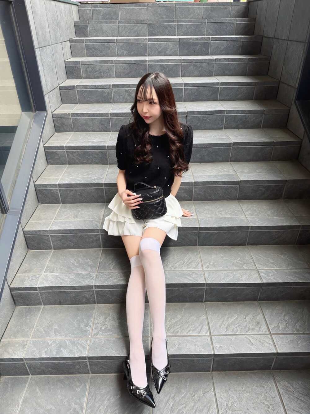 ブラック系のニット/セーター、ホワイト系のスカート、ブラック系のショルダーバッグを着用したレディースの春コーディネートの2枚目の写真