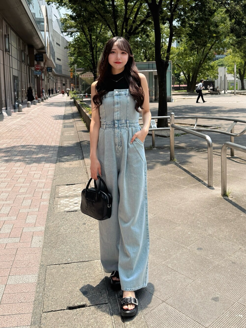 ブルー系のサロペット/オーバーオール、ブラック系のハンドバッグ、ブラック系のサンダルを着用したレディースの夏コーディネートの2枚目の写真