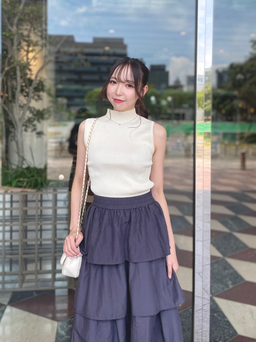 ホワイト系のニット/セーター、ホワイト系のショルダーバッグ、グレー系のスカートを着用したレディースの夏コーディネートの2枚目の写真