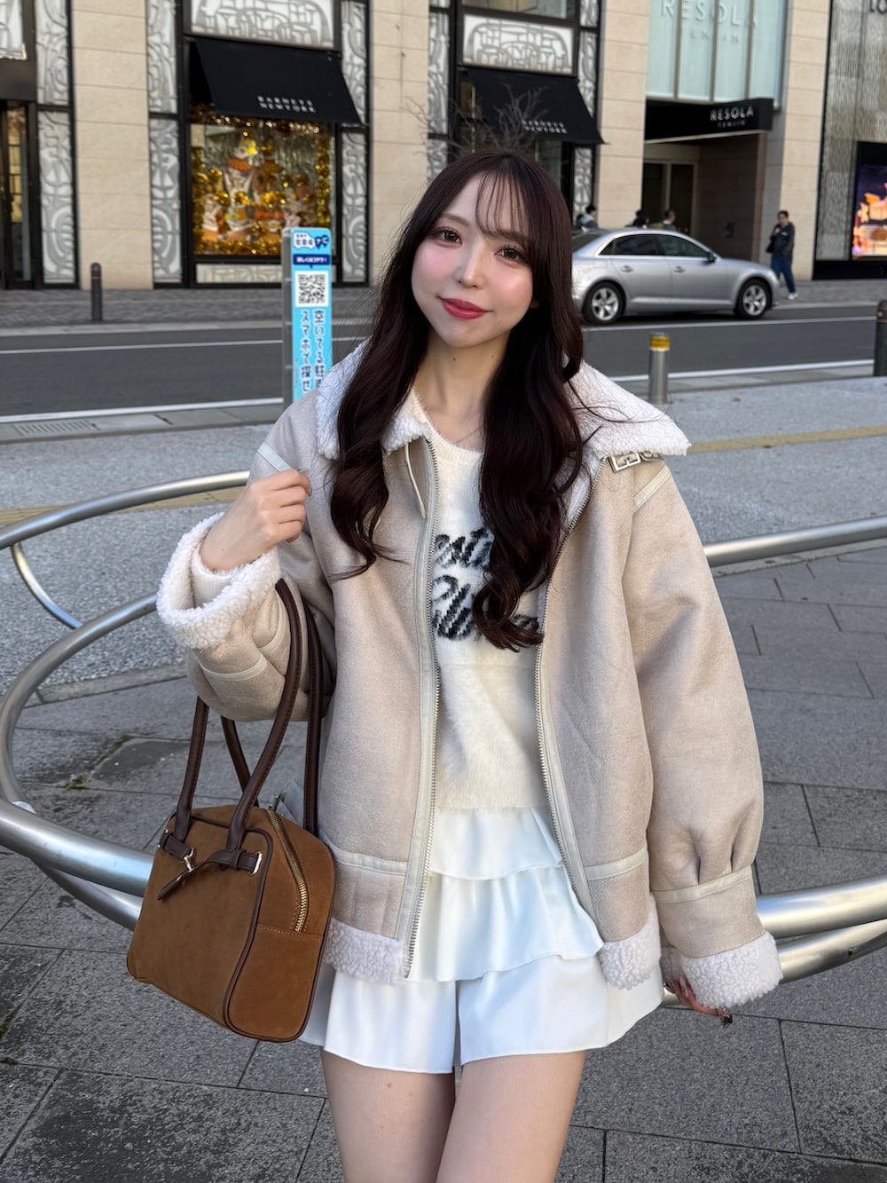 ホワイト系のブルゾン、ホワイト系のスカート、イエロー系のハンドバッグを着用したレディースの秋コーディネートの3枚目の写真