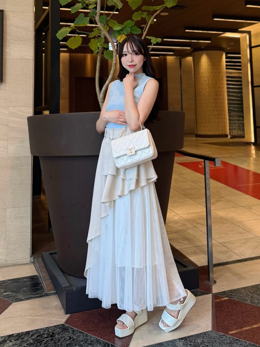 ベージュ系のスカート、ブルー系のニット/セーター、ホワイト系のショルダーバッグを着用したレディースの夏コーディネートの2枚目の写真