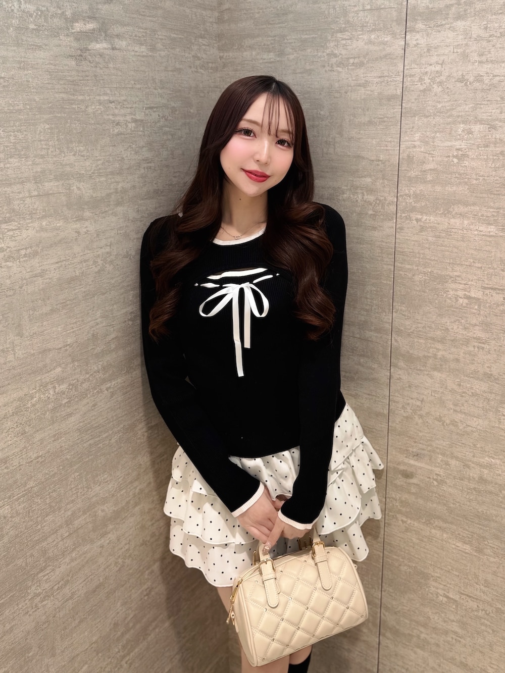 ホワイト系のボストンバッグ、ホワイト系のスカート、ブラック系のニット/セーターを着用したレディースの春コーディネートの2枚目の写真