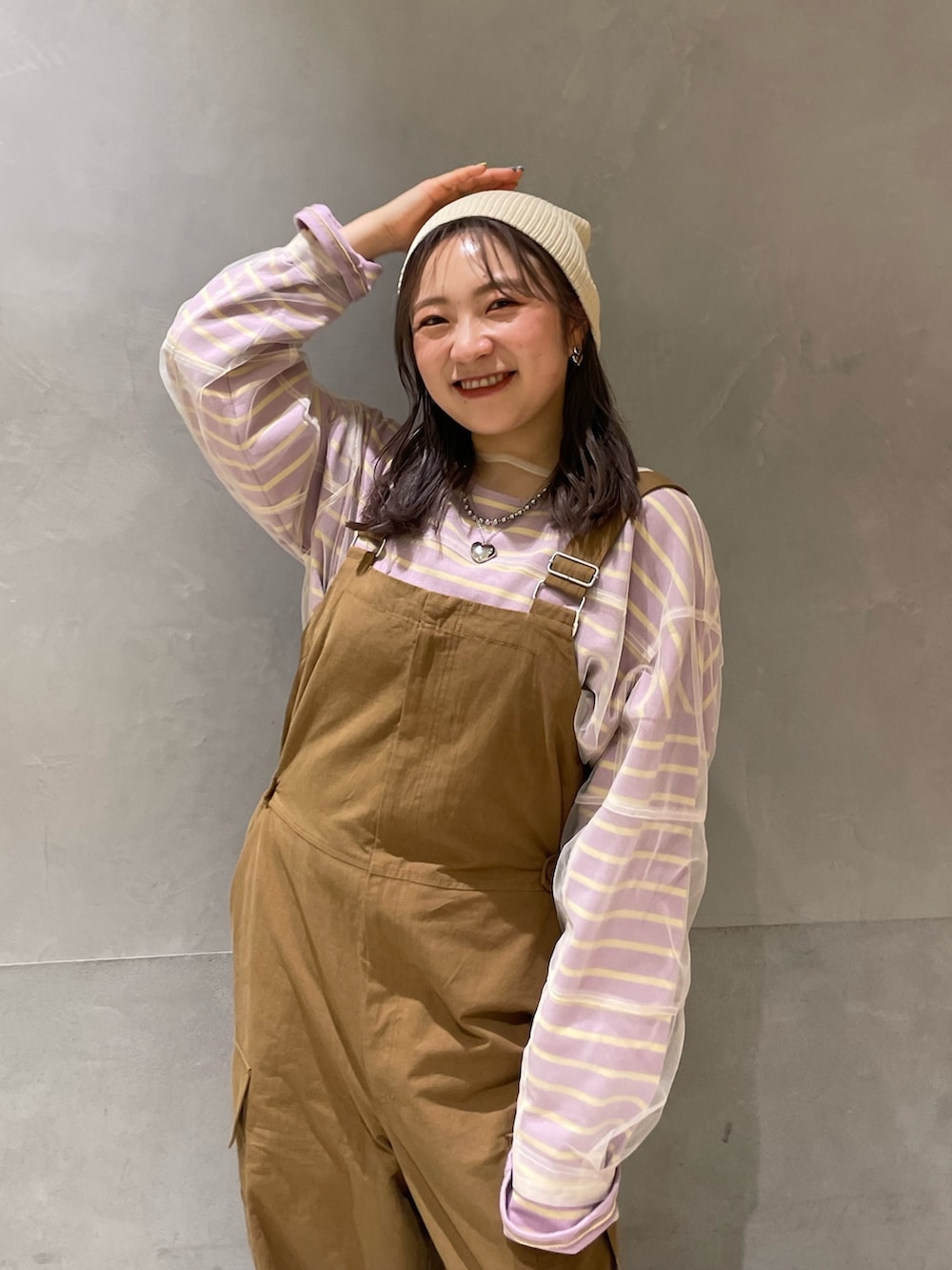 ベージュ系のステンカラーコート、イエロー系のつなぎ/オールインワン、パープル系のTシャツ/カットソーを着用したレディースの冬コーディネートの8枚目の写真