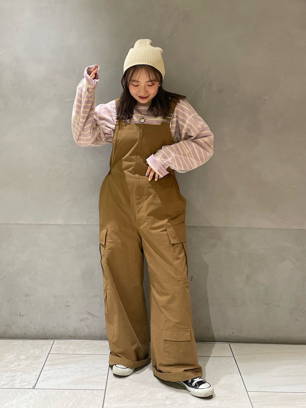 ベージュ系のステンカラーコート、イエロー系のつなぎ/オールインワン、パープル系のTシャツ/カットソーを着用したレディースの冬コーディネートの5枚目の写真