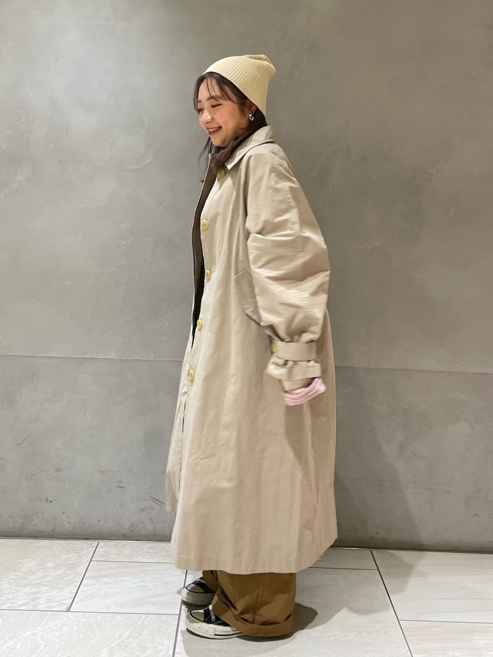 ベージュ系のステンカラーコート、イエロー系のつなぎ/オールインワン、パープル系のTシャツ/カットソーを着用したレディースの冬コーディネートの3枚目の写真