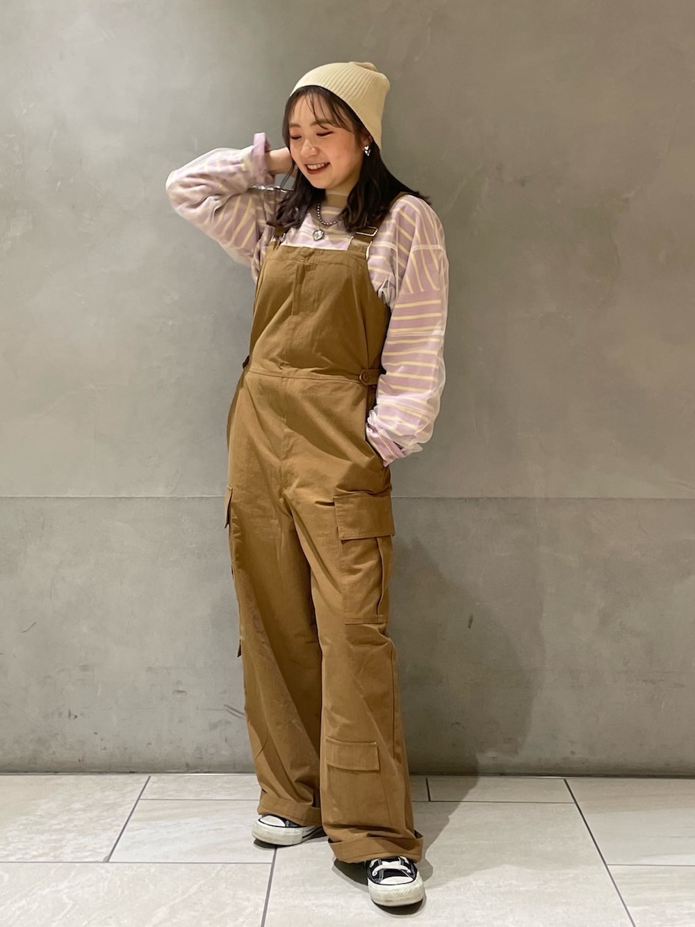 ベージュ系のステンカラーコート、イエロー系のつなぎ/オールインワン、パープル系のTシャツ/カットソーを着用したレディースの冬コーディネートの6枚目の写真