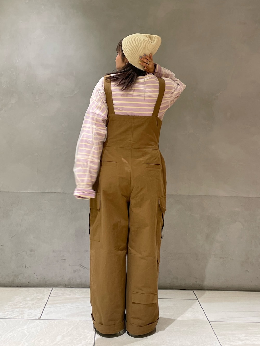 ベージュ系のステンカラーコート、イエロー系のつなぎ/オールインワン、パープル系のTシャツ/カットソーを着用したレディースの冬コーディネートの7枚目の写真