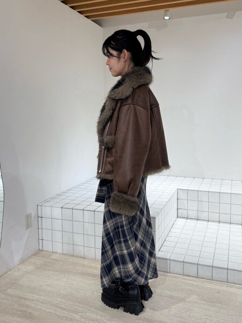 ブルー系のスカート、ブラウン系のブルゾン、ブラック系のブーツを着用したレディースの秋コーディネートの2枚目の写真