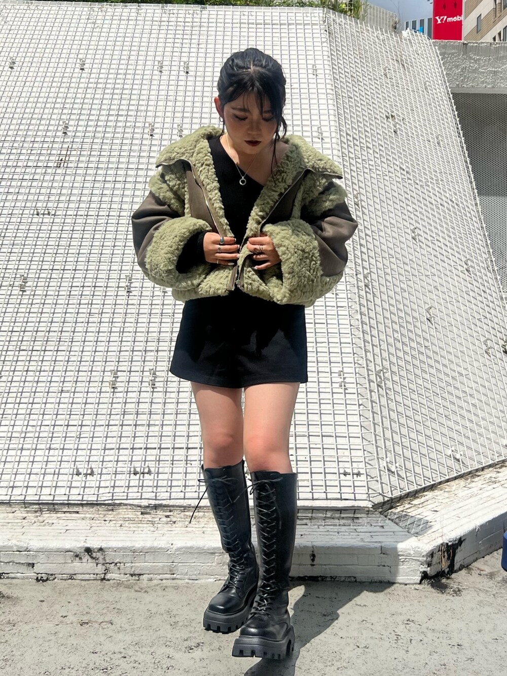 ブラック系のその他パンツ、ブラック系のブーツ、グリーン系のムートンコートを着用したレディースの夏コーディネートの2枚目の写真