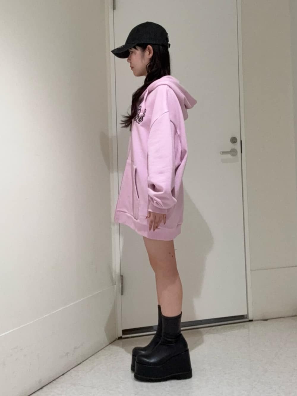 ブラック系のブーツ、ピンク系のパーカー、ブラック系のキャップを着用したレディースの春コーディネートの2枚目の写真