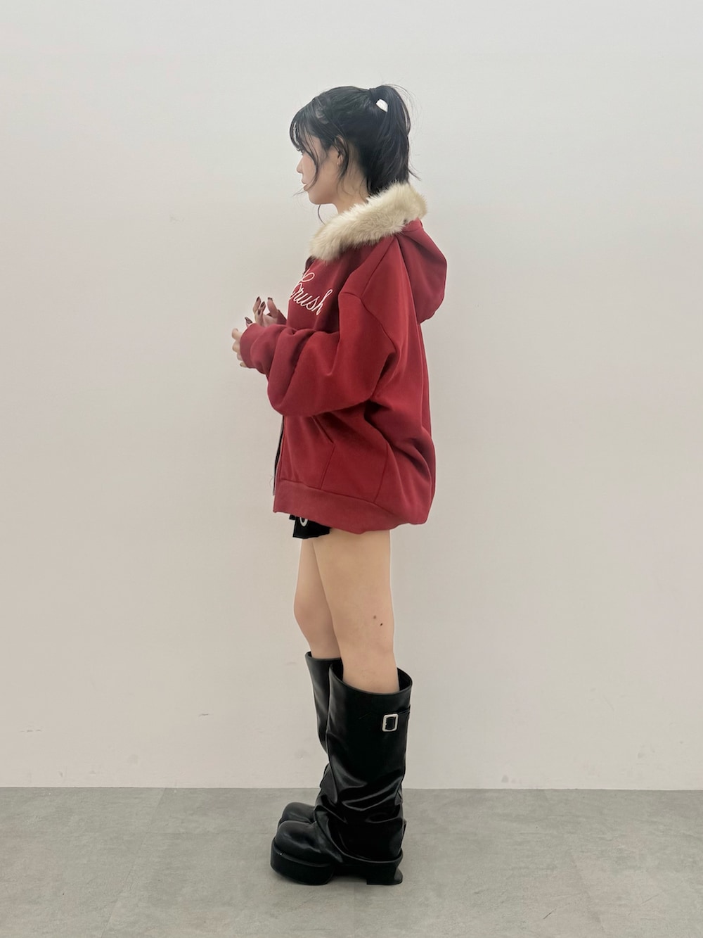 レッド系のパーカー、ブラック系のスカート、ブラック系のブーツを着用したレディースの秋コーディネートの2枚目の写真