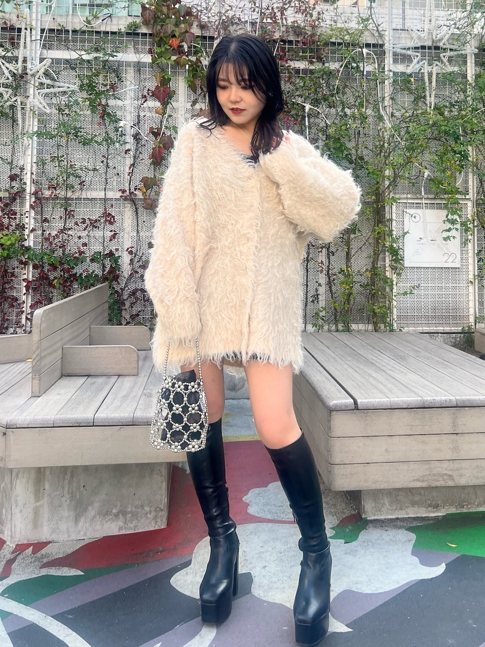 ホワイト系のカーディガン/ボレロ、ブラック系のブーツ、シルバー系のハンドバッグを着用したレディースの冬コーディネートの2枚目の写真