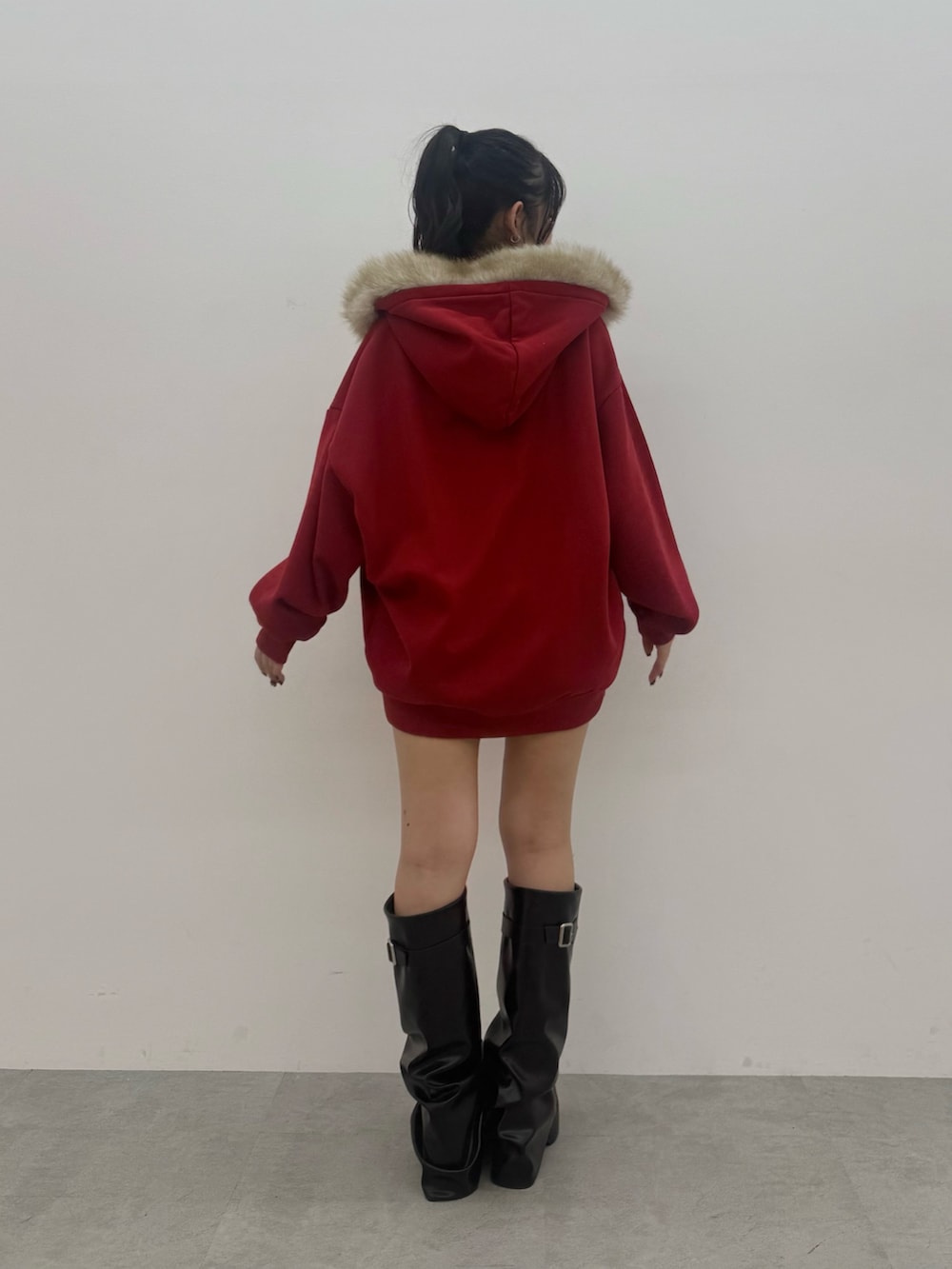 レッド系のパーカー、ブラック系のスカート、ブラック系のブーツを着用したレディースの秋コーディネートの3枚目の写真