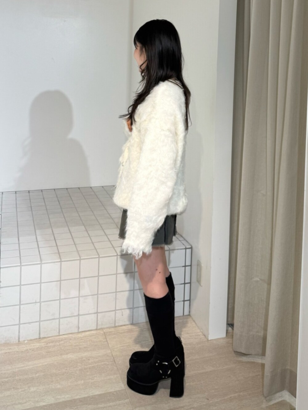 グレー系のスカート、ブラック系のブーツ、ホワイト系のカーディガン/ボレロを着用したレディースの秋コーディネートの2枚目の写真