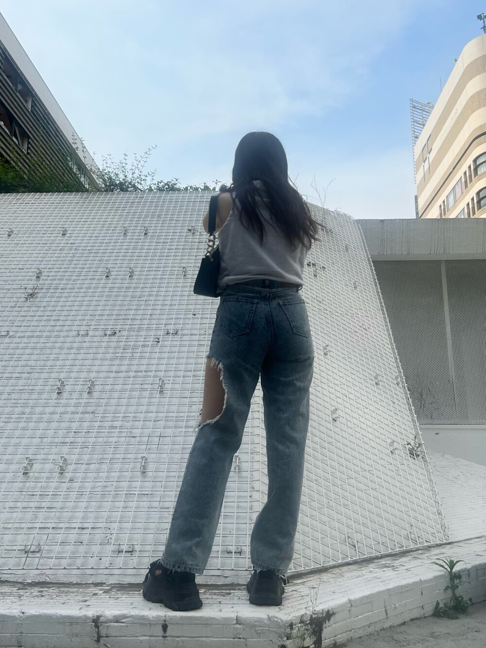 ブルー系のデニムパンツ、ブラック系のハンドバッグ、グレー系のタンクトップを着用したレディースの夏コーディネートの4枚目の写真