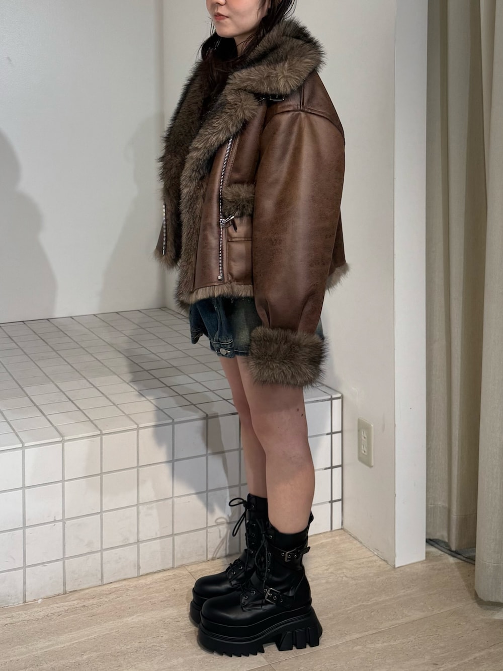 ブラウン系のブルゾン、ブルー系のデニムスカート、ブラック系のブーツを着用したレディースの秋コーディネートの2枚目の写真