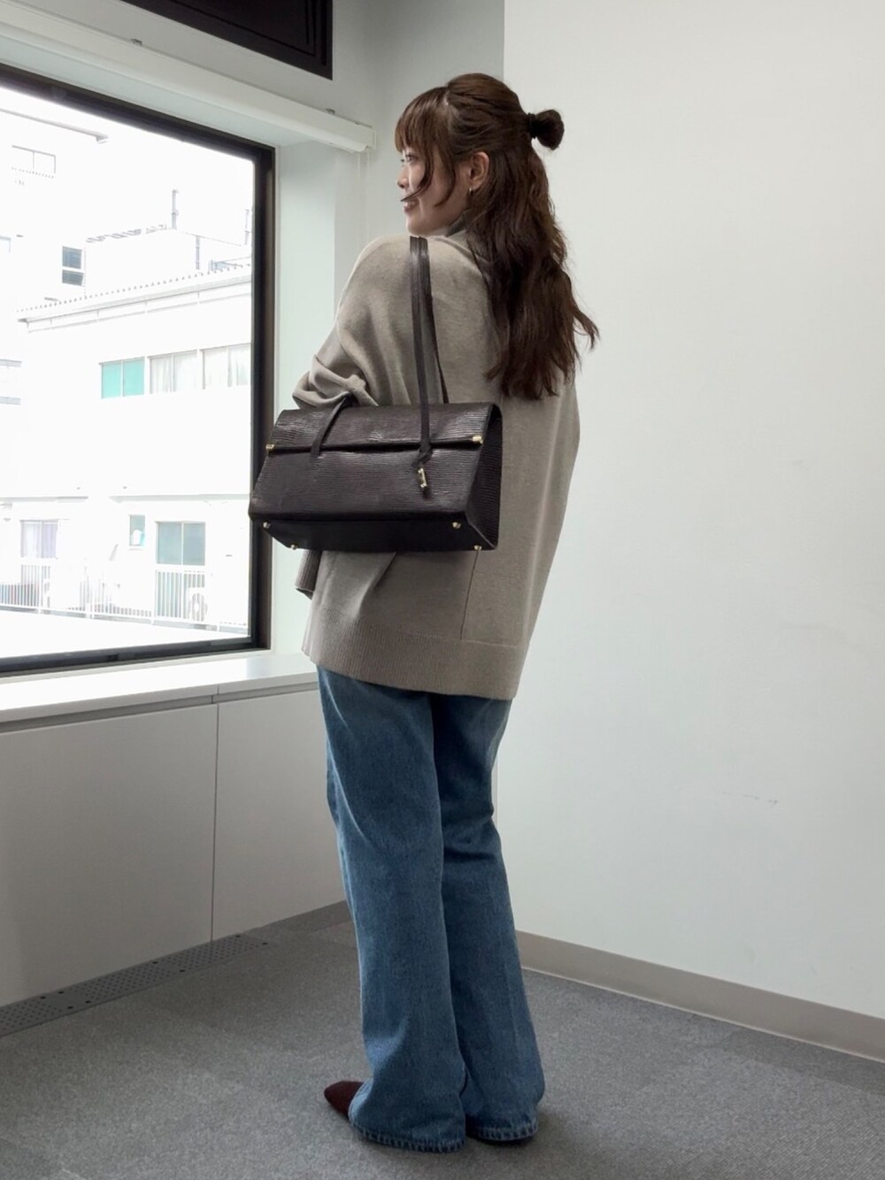 ブルー系のデニムパンツ、ベージュ系のニット/セーター、ブラウン系のトートバッグを着用したレディースの秋コーディネートの2枚目の写真