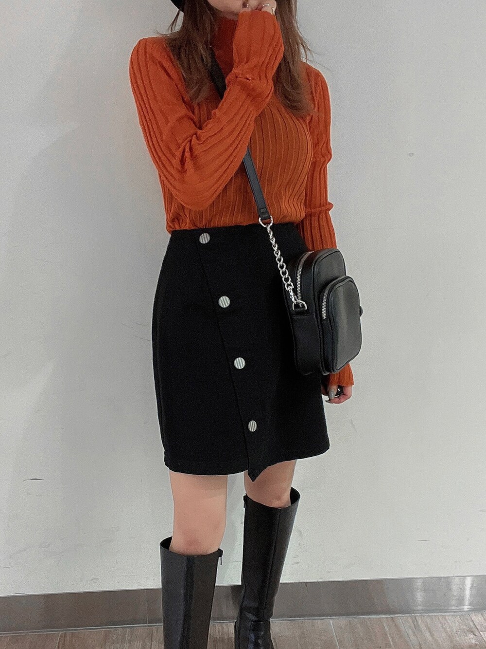 オレンジ系のニット/セーター、ブラック系のスカート、ブラック系のブーツを着用したレディースの秋コーディネートの3枚目の写真