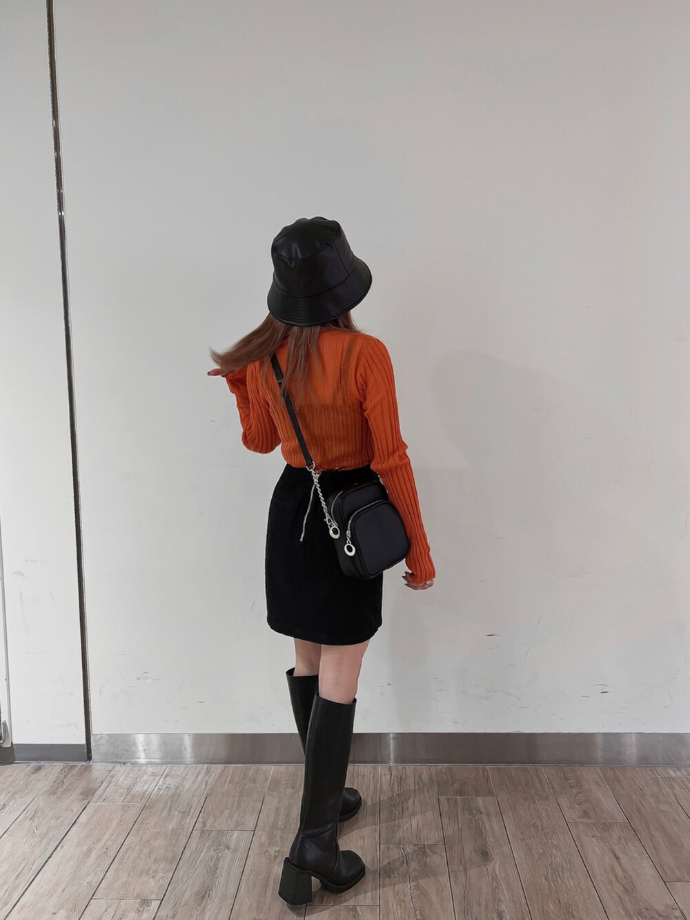 オレンジ系のニット/セーター、ブラック系のスカート、ブラック系のブーツを着用したレディースの秋コーディネートの2枚目の写真