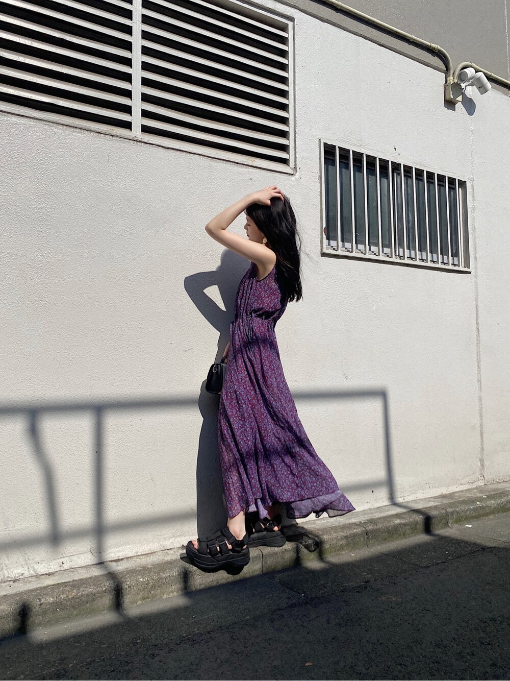 パープル系のワンピース、ブラック系のサンダル、ゴールド系のイヤリングを着用したレディースの夏コーディネートの2枚目の写真