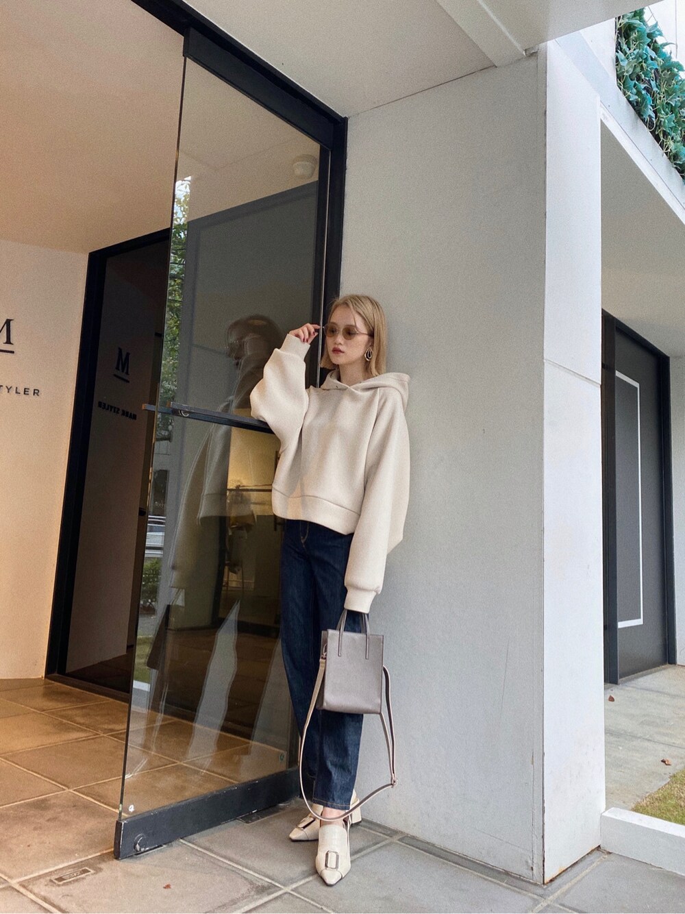 ベージュ系のショルダーバッグ、ホワイト系のパーカー、ブルー系のデニムパンツを着用したレディースの秋コーディネートの4枚目の写真