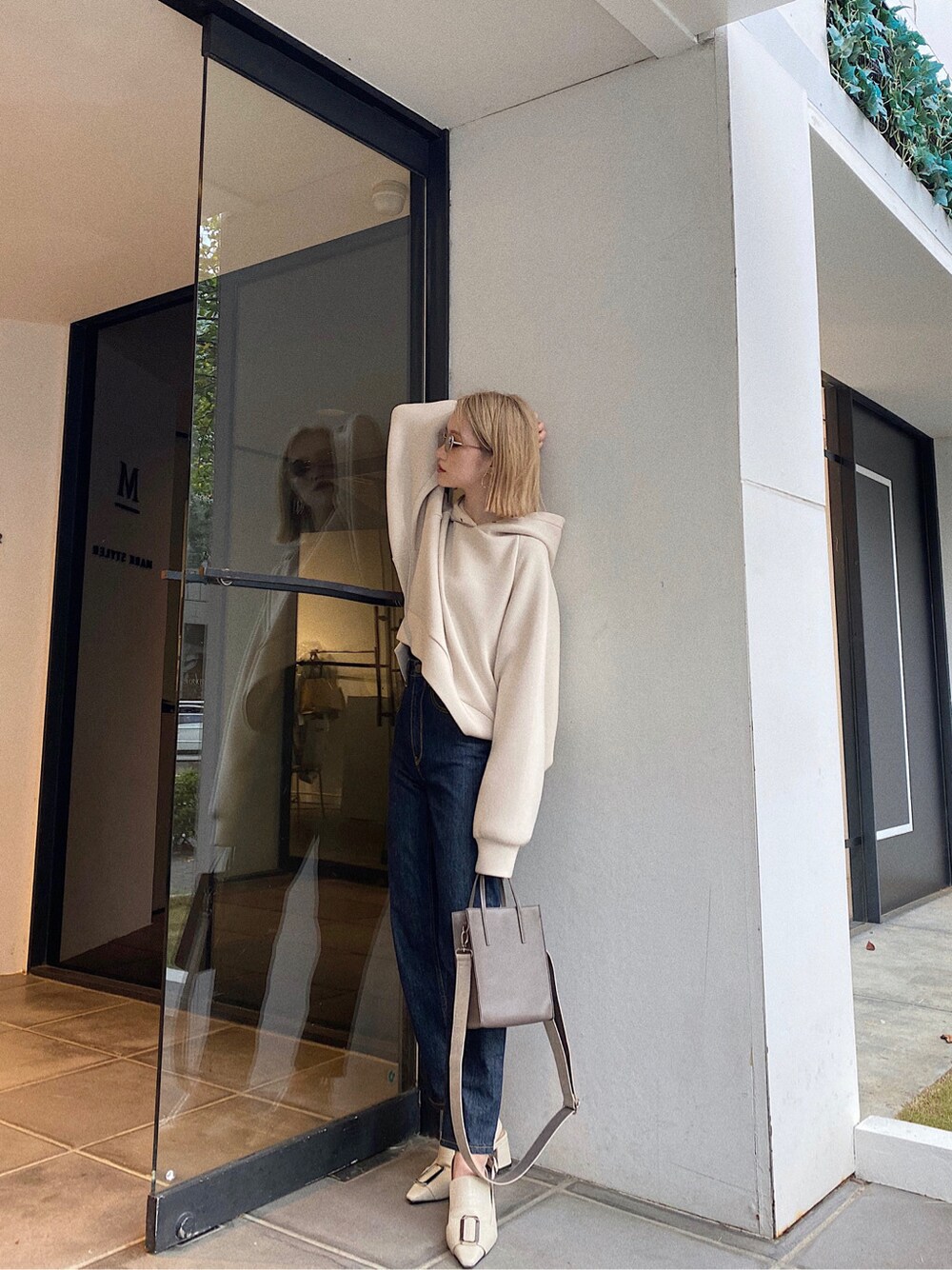 ベージュ系のショルダーバッグ、ホワイト系のパーカー、ブルー系のデニムパンツを着用したレディースの秋コーディネートの2枚目の写真