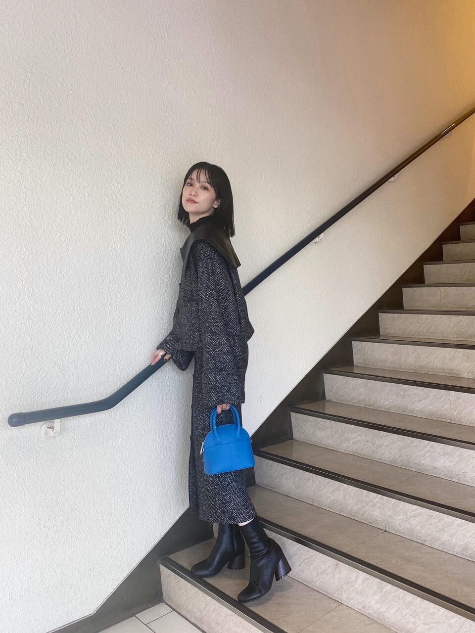 ブラック系のブーツ、ブルー系のハンドバッグ、ブラック系のスカートを着用したレディースの秋コーディネートの3枚目の写真