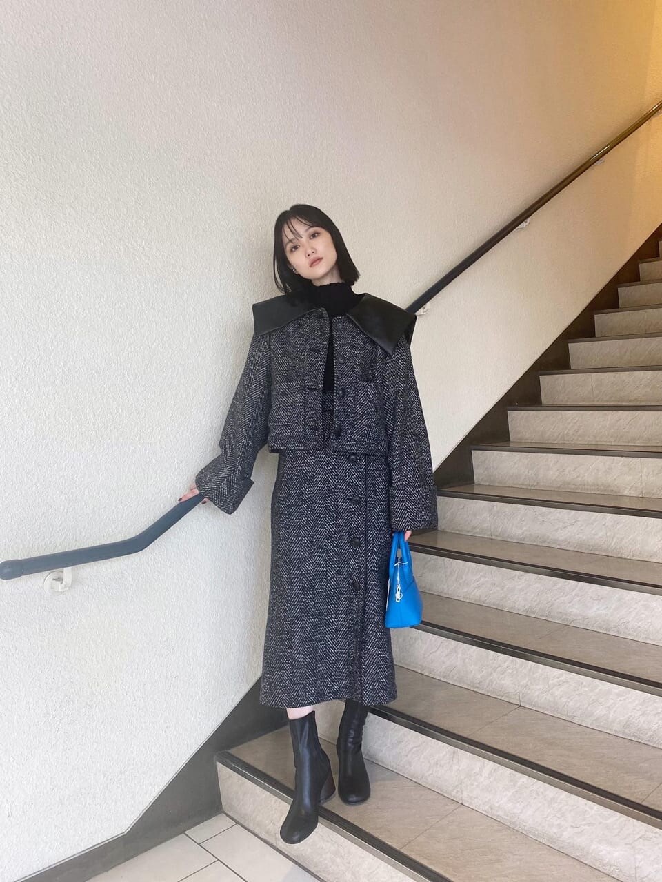 ブラック系のブーツ、ブルー系のハンドバッグ、ブラック系のスカートを着用したレディースの秋コーディネートの2枚目の写真