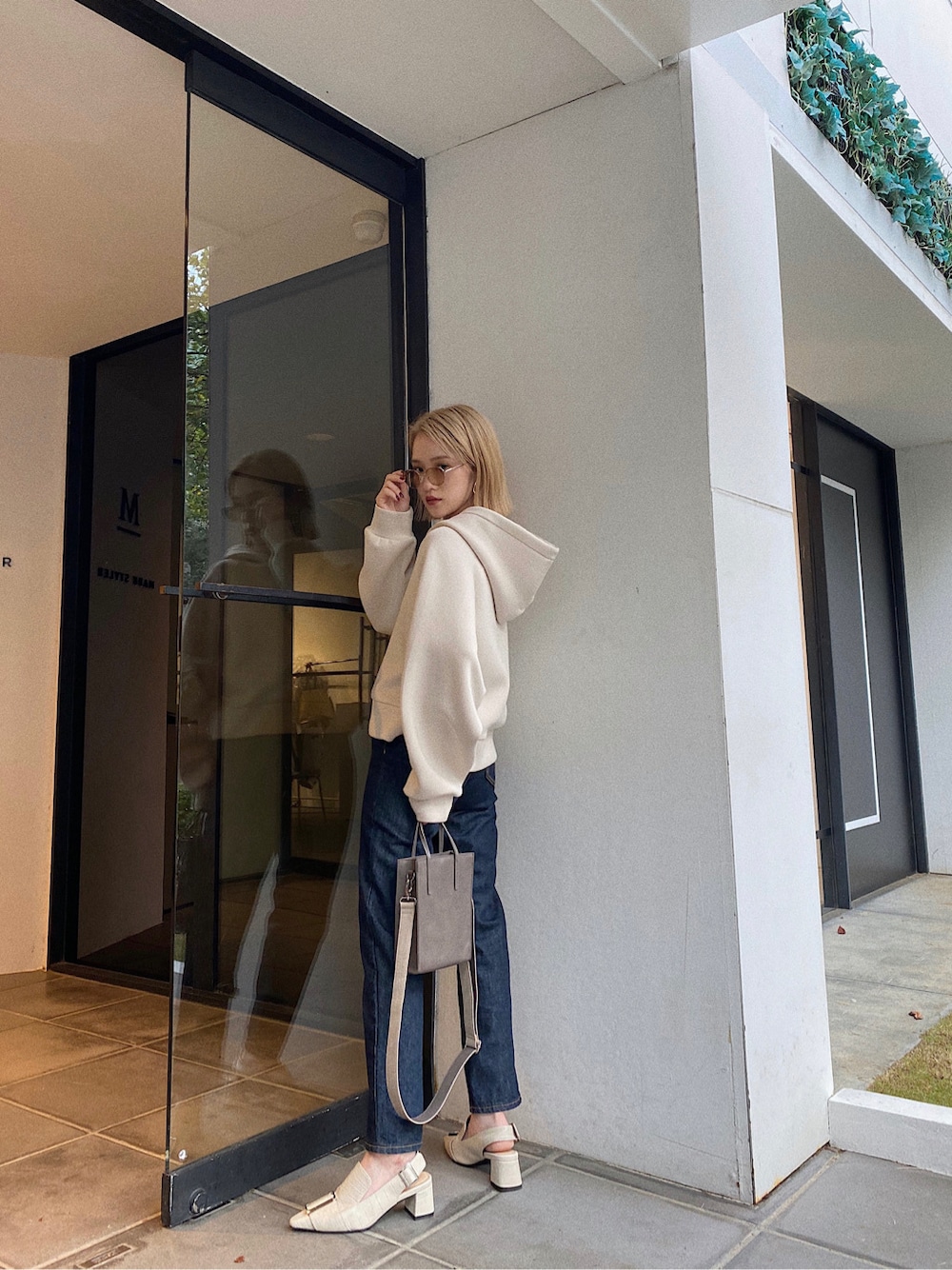 ベージュ系のショルダーバッグ、ホワイト系のパーカー、ブルー系のデニムパンツを着用したレディースの秋コーディネートの3枚目の写真