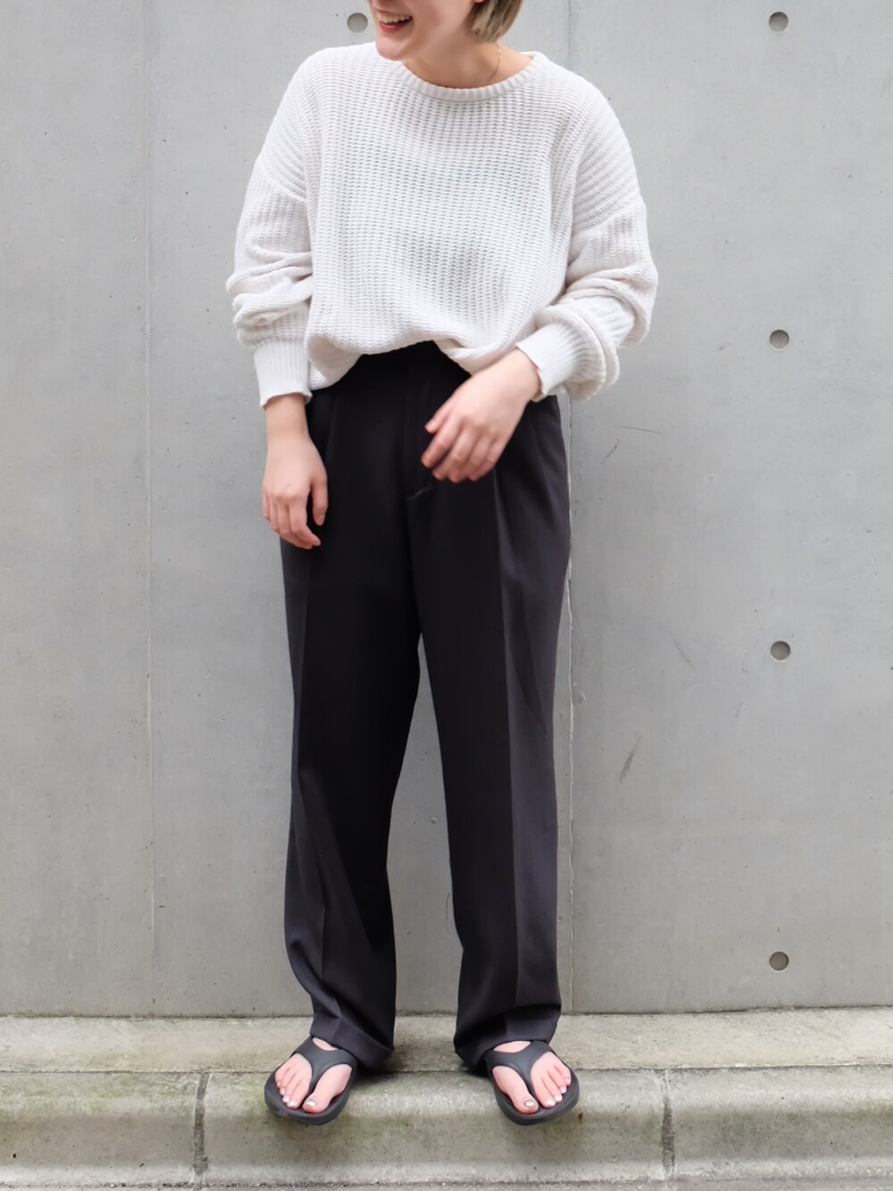 グレー系のスラックス、ブラック系のサンダル、ホワイト系のニット/セーターを着用したレディースの秋コーディネートの2枚目の写真