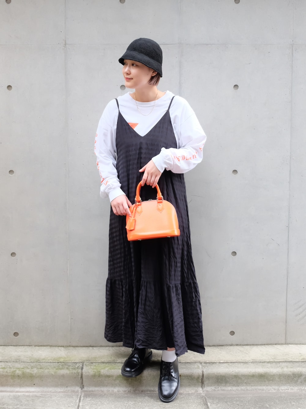 ブラック系のブーツ、ブラック系のワンピース、オレンジ系のハンドバッグを着用したレディースの秋コーディネートの2枚目の写真