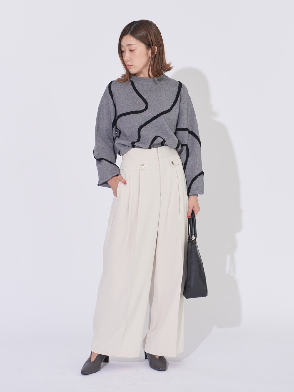 グレー系のニット/セーター、ホワイト系のその他パンツ、ブラック系のトートバッグを着用したレディースの冬コーディネートの2枚目の写真