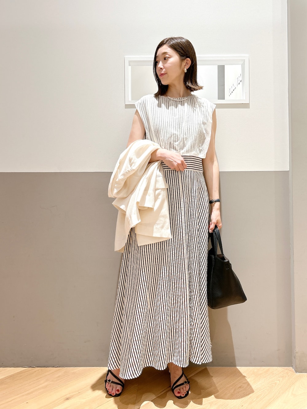 ホワイト系のテーラードジャケット、ホワイト系のワンピース、ブラック系のサンダルを着用したレディースの春コーディネートの2枚目の写真