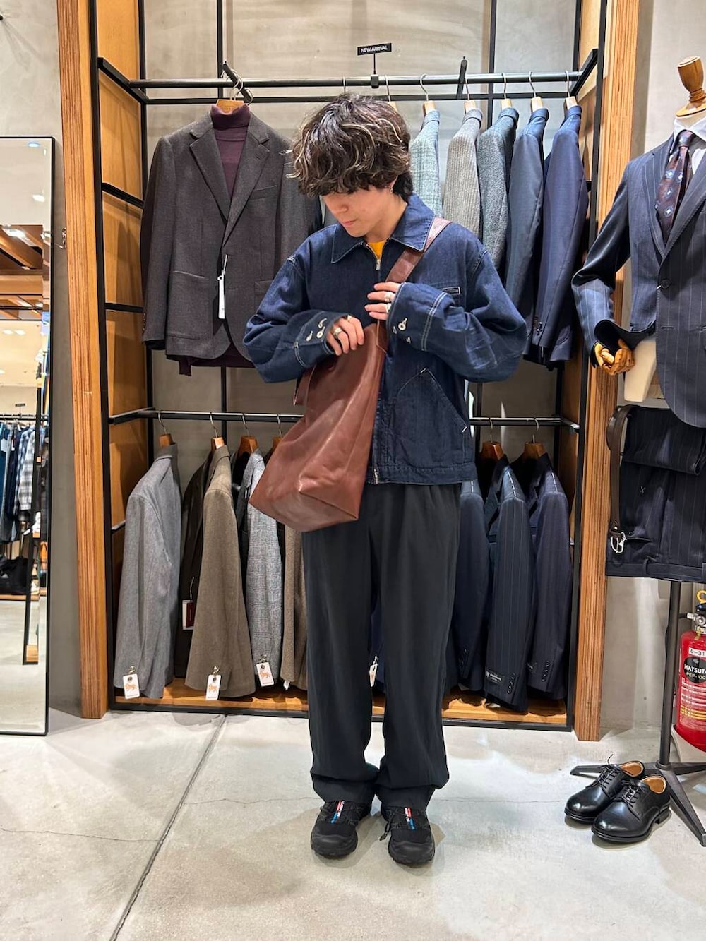 ブラウン系のトートバッグ、ブラック系のスニーカー、ブラック系のデニムパンツを着用したメンズの秋コーディネートの3枚目の写真