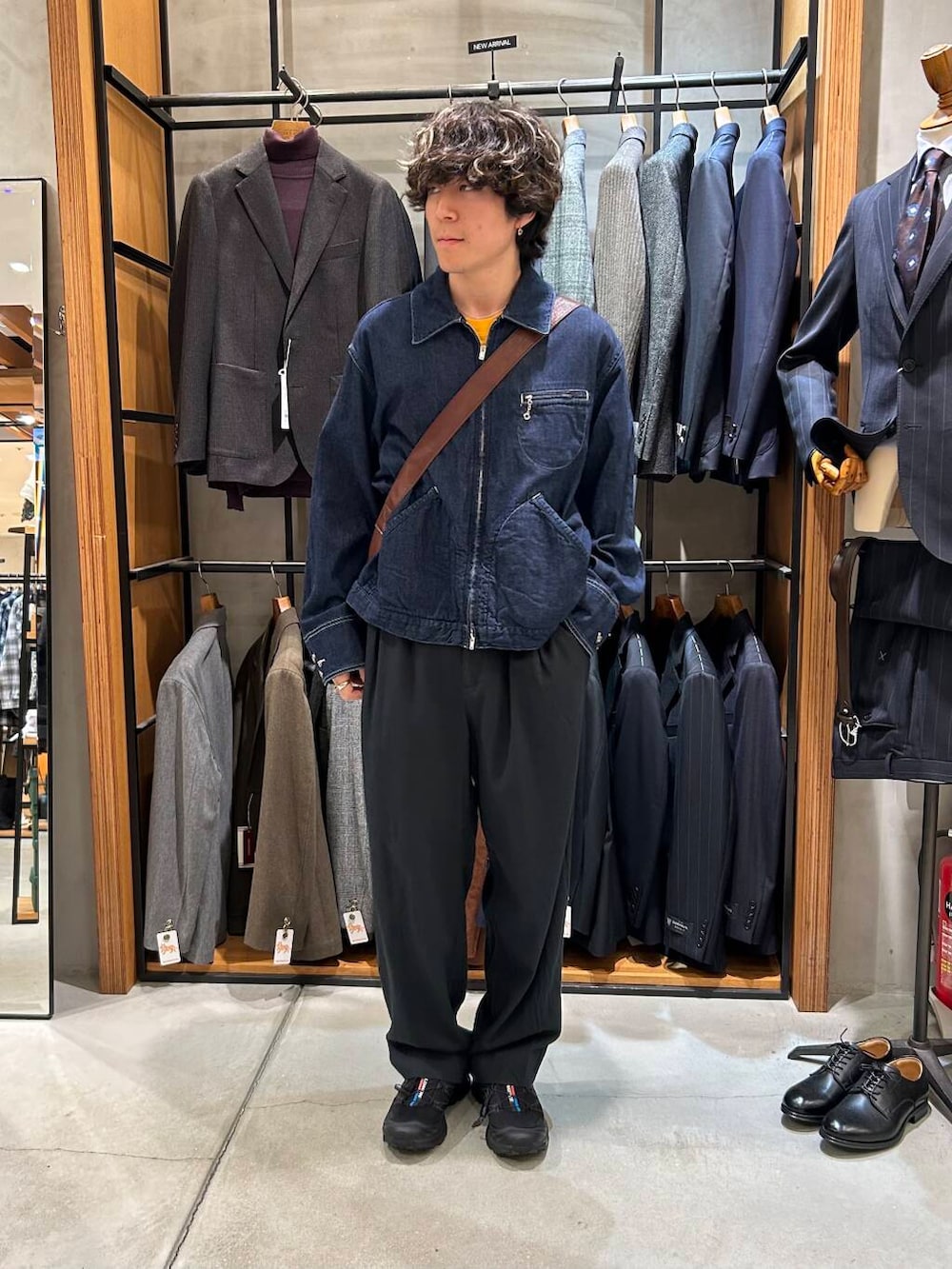 ブラウン系のトートバッグ、ブラック系のスニーカー、ブラック系のデニムパンツを着用したメンズの秋コーディネートの2枚目の写真